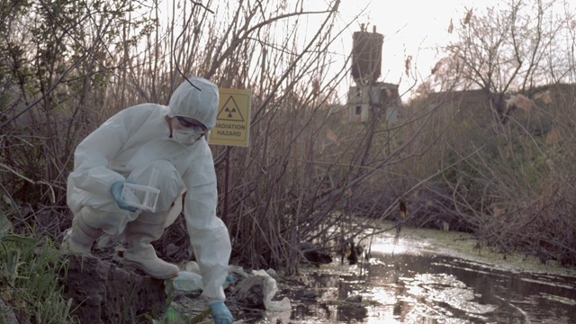 放射性区域，危险品化学家进入防护服，在受污染的湖泊中采集受感染的水样进行检测，用指针标记辐射危害视频素材