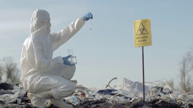 生物危害，危险品化学家进入防护服，在试管中采集受感染的垃圾样本，在垃圾填埋场上用指针标记生物危害视频素材
