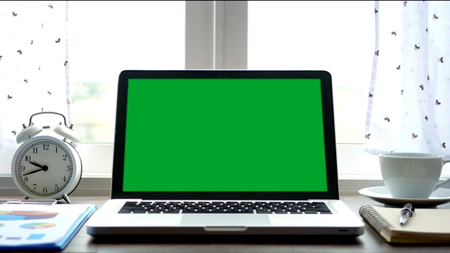 4 k。笔记本电脑与一个绿色屏幕色度键设置在工作办公室的桌子上，靠近窗户与白色窗帘吹视频下载