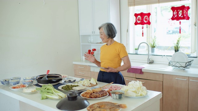 愉快的亚洲高级妇女在家烹饪平板电脑视频素材