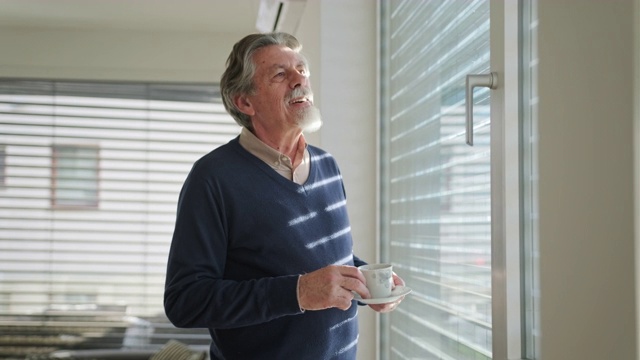 一个资深白人男子站在窗边喝着咖啡视频下载