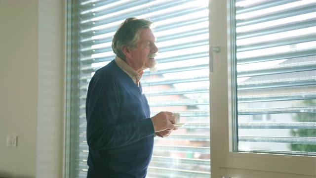 一个资深白人男子站在窗边喝着咖啡视频素材