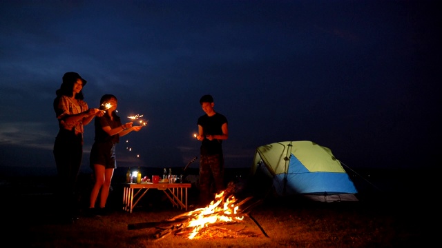 场景慢镜头一群青少年亚洲人一起享受帐篷前的营火和在湖边放烟花在暑假。他们是快乐的，有乐趣的假期，放松的时刻。青少年自然户外日常生活的概念视频素材