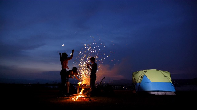 场景慢镜头一群青少年亚洲人一起享受帐篷前的营火和在湖边放烟花在暑假。他们是快乐的，有乐趣的假期，放松的时刻。青少年自然户外日常生活的概念视频下载