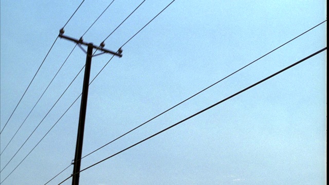向上的角度驱动pov 3/4右向前的电源或电话线。电线杆。可能是在乡村或农村地区。蓝色的天空。视频下载