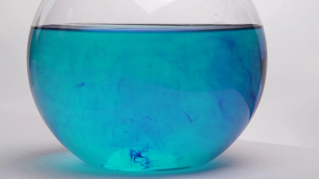 深蓝色化学试剂的扩散。瓶中的液体变色。瓶中化学反应的特写。孤立，在白色背景上视频下载