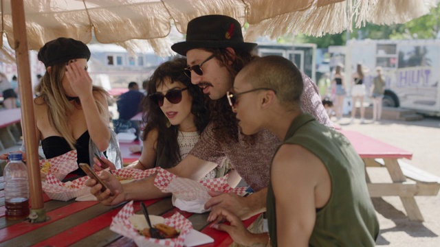 一群朋友围坐在餐车节的野餐桌旁看智能手机。视频素材