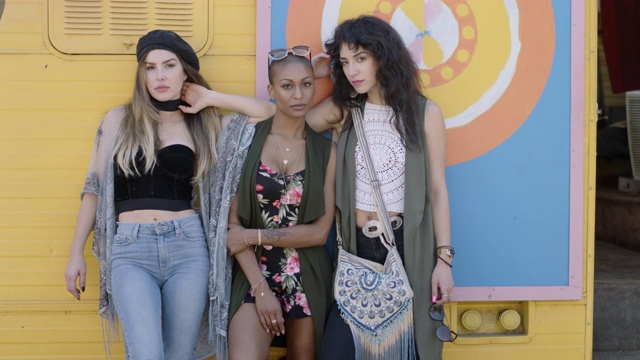 在户外节日上，三个美丽、强悍的年轻女子抬头盯着镜头，站在五颜六色的餐车前。视频素材