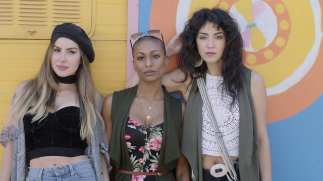 三名美丽、强悍的年轻女子在五彩缤纷的街头艺术背景前盯着镜头。视频下载
