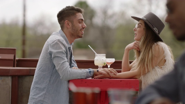 时髦的年轻夫妇手牵着手，在户外露台上喝着鸡尾酒大笑。视频素材