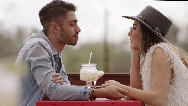时髦的年轻夫妇手牵着手，在户外露台上喝着鸡尾酒聊天。视频素材