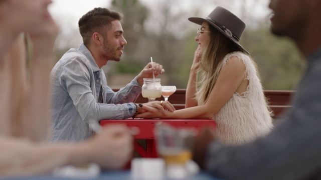 时髦的年轻夫妇喝着鸡尾酒，在户外酒吧的露台上聊天。视频素材