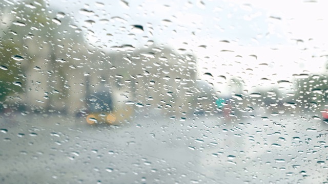 汽车挡风玻璃上的雨滴。模糊的城市街道和车流。视频素材