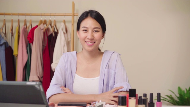 美妆博主坐在写字板前拍摄美妆视频。快乐美丽的年轻亚洲女子用化妆品点评化妆教程在社交网络直播。视频素材