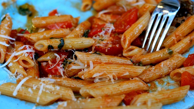 意大利面配上美味的番茄酱，肉，帕尔马干酪和西红柿，用叉子和蓝色的盘子吃。视频素材