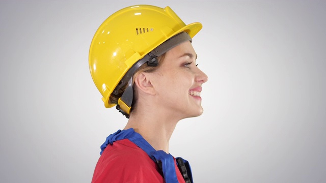 戴着黄色安全帽的年轻女工程师在渐变背景下微笑着行走视频下载