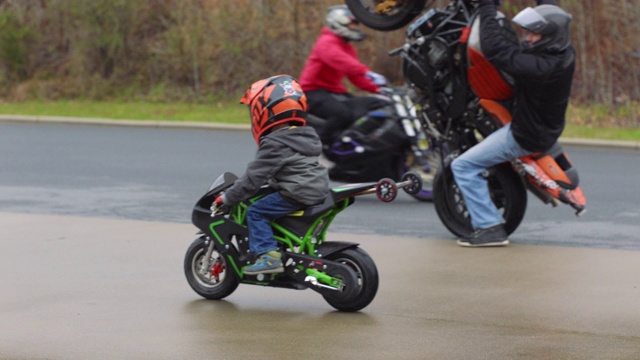 小男孩骑着一辆儿童尺寸的特技自行车，旁边是一名专业特技摩托车骑手，他在自行车前轮前倾视频下载