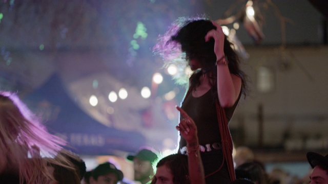 在一个流行音乐节上，一名千禧一代的波西米亚女子骑在她的另一半的肩膀上摇滚起来视频素材