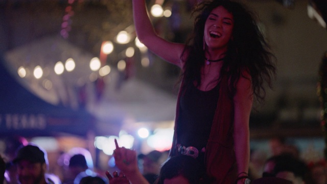 SLO MO:在一个流行音乐节上，一名千禧一代的波西米亚女子骑在她的另一半的肩膀上，双手向空中挥舞视频素材
