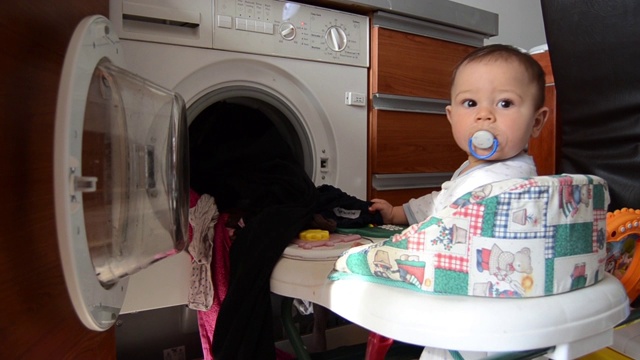 可爱的六个月大的小男孩帮助洗衣服-把洗好的衣服从洗衣机里拉出来视频素材
