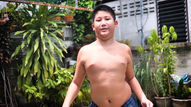 胖的十来岁的男孩在后院户外摇动他的肚子，慢动作。视频下载