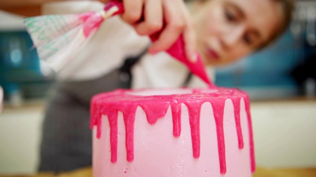 女甜品师用糕点包装饰手工制作的粉色奶油蛋糕，上面有滴莓酱糖霜，特写锁定镜头视频素材