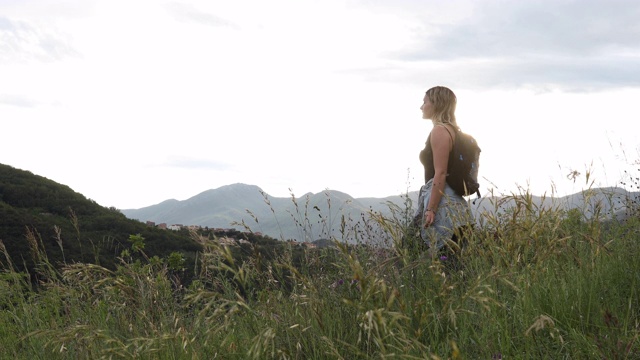 女徒步旅行者走进草地，眺望远处的群山视频素材