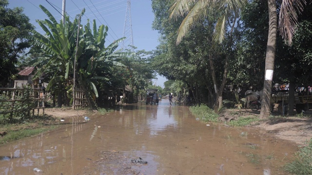 一辆摩托车穿过被水淹没的街道村庄的后视图。视频素材