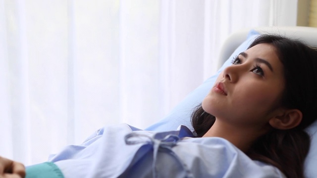 女病人住院悲伤的年轻女子躺在病房里望着窗外。一个人。担心视频素材