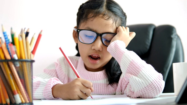小亚洲女孩用铅笔在纸上写作业，带着幸福的微笑为教育理念选择焦点浅的景深视频素材