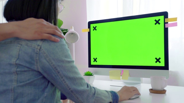 年轻的成年妇女在她的办公桌前和她的丈夫在一台模拟绿屏的电脑上工作。过肩镜头。她坐在家里的书桌前。视频素材