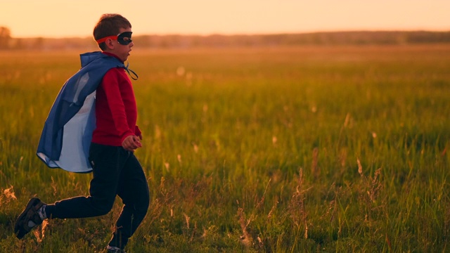 一个穿着西装戴着超级英雄面具的男孩在日落的草地上跑过田野视频素材