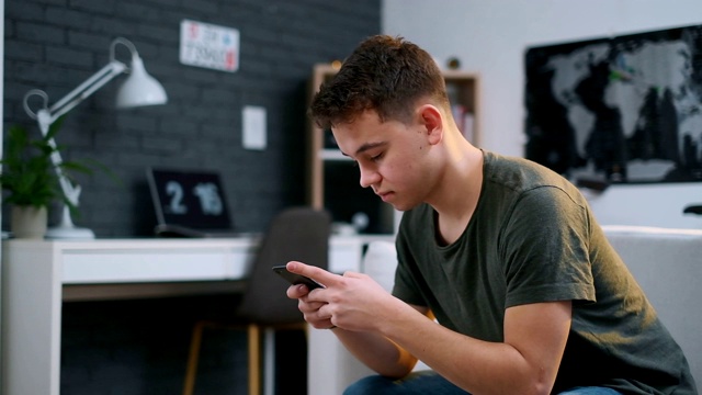 一个青少年坐在一个时髦的房间的沙发上专注于他的手机的侧面特写视频素材