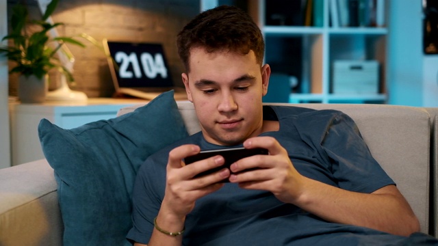 一个小男孩躺在沙发上玩手机游戏的特写视频视频素材