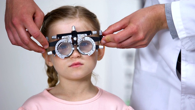 眼科医生给小女孩选择屈光度，使用光学设备视频素材