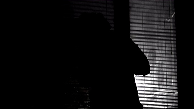 一个孤独的女人在夜晚透过百叶窗看着暴风雨，看着外面视频素材