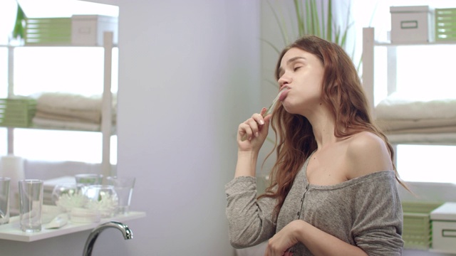 年轻女子用牙刷刷牙，在浴室镜子前摆姿势视频素材