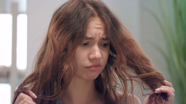 不快乐的年轻女子触摸和看在镜子浴室的头发末端视频下载