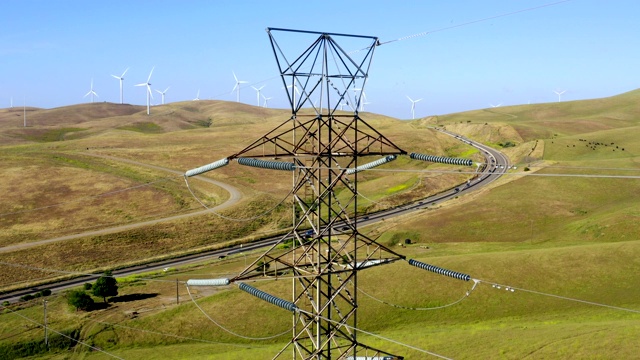 鸟瞰高压线，输电塔和风力涡轮机在一个阳光明媚的一天在北加州的田地。电力工业和自然环境的概念。视频素材