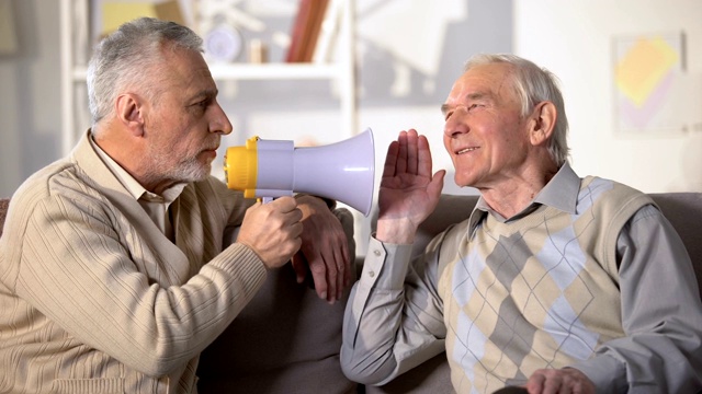 年长男性用扩音器对耳聋的老朋友说话，健康问题，特写视频素材