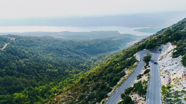 空中电影无人机在晴朗的蓝天下拍摄的蛇形山道。美丽的山谷和湖在远处。俯瞰夏天的绿色乡村。视频素材