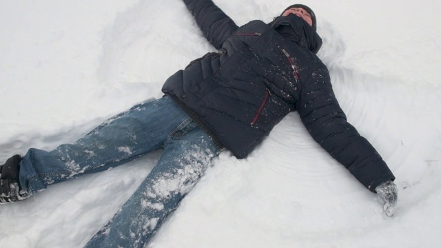 一个小男孩躺在雪地里，在冬天的森林里玩耍，美丽的风景和积雪的冷杉树视频下载
