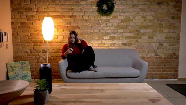 年轻漂亮的白人女性使用手机的特写肖像，而坐在一个舒适的公寓室内的沙发上视频素材