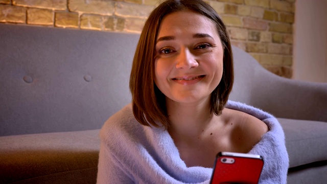 年轻迷人的白人女性的特写镜头使用手机看相机和微笑在舒适的家里室内视频素材