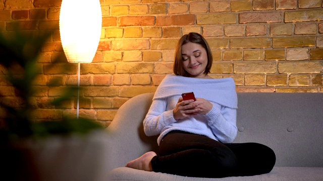 年轻开朗的白人女性的特写镜头在电话上发短信，微笑着愉快地在家里放松视频素材