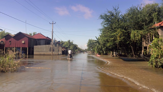 一辆摩托车穿过被水淹没的街道村庄的后视图。视频素材