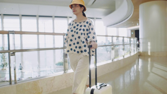 年轻的亚洲女人穿着高跟鞋走在机场，用轮子推着行李箱视频素材
