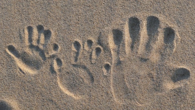 在日落时分的沙滩上，成人和儿童的手留下了手印视频下载