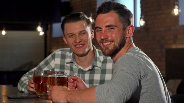 在酒吧里喝啤酒的快乐的男人对着镜头微笑视频下载