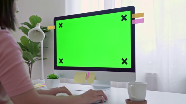 年轻的成年人在她的办公桌前工作在一台模拟绿色屏幕的电脑上。过肩镜头。她坐在家里的书桌前。视频素材